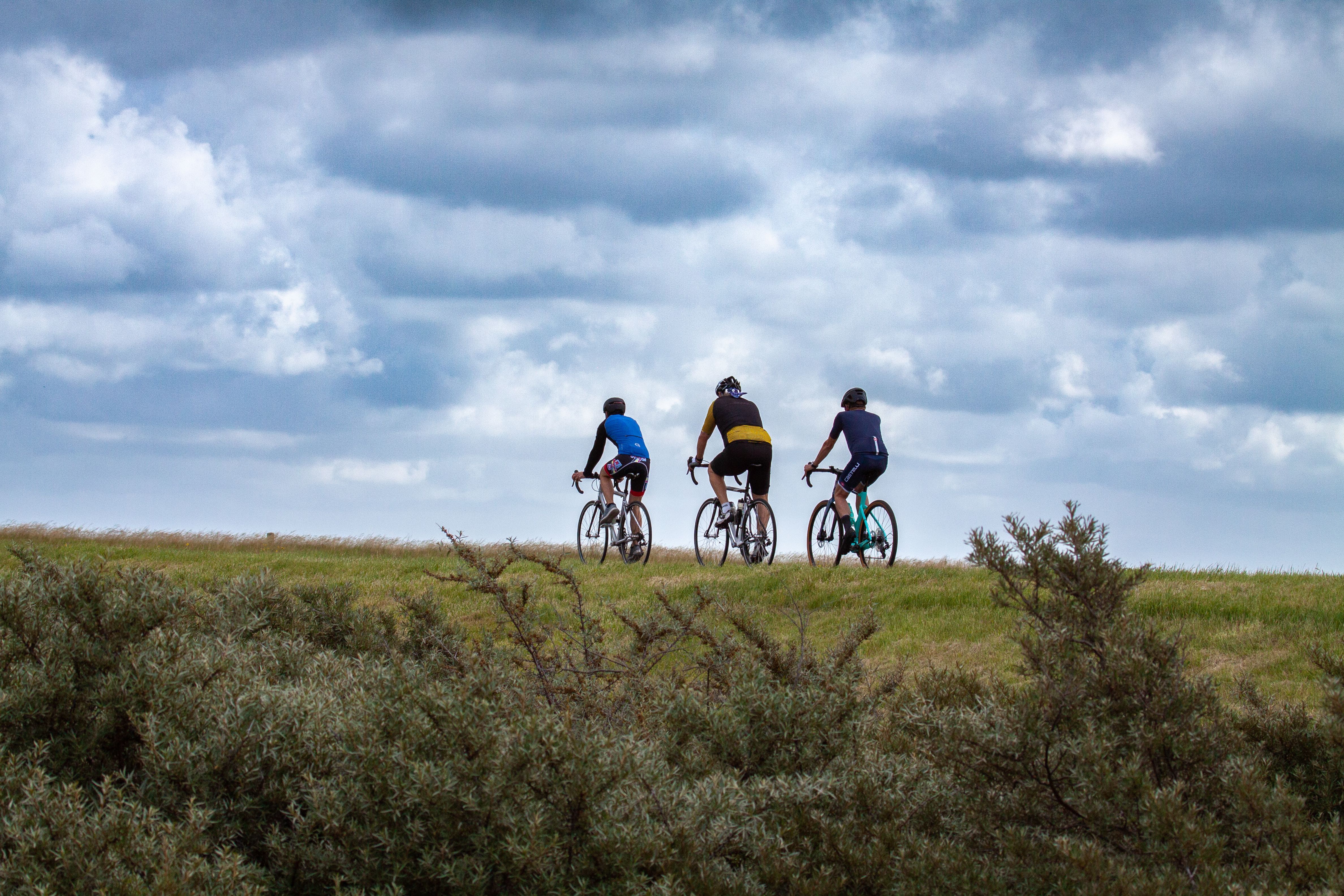 Three cyclists enjoy a scenic ride in Kamperland, Netherlands under a dramatic cloudy sky.