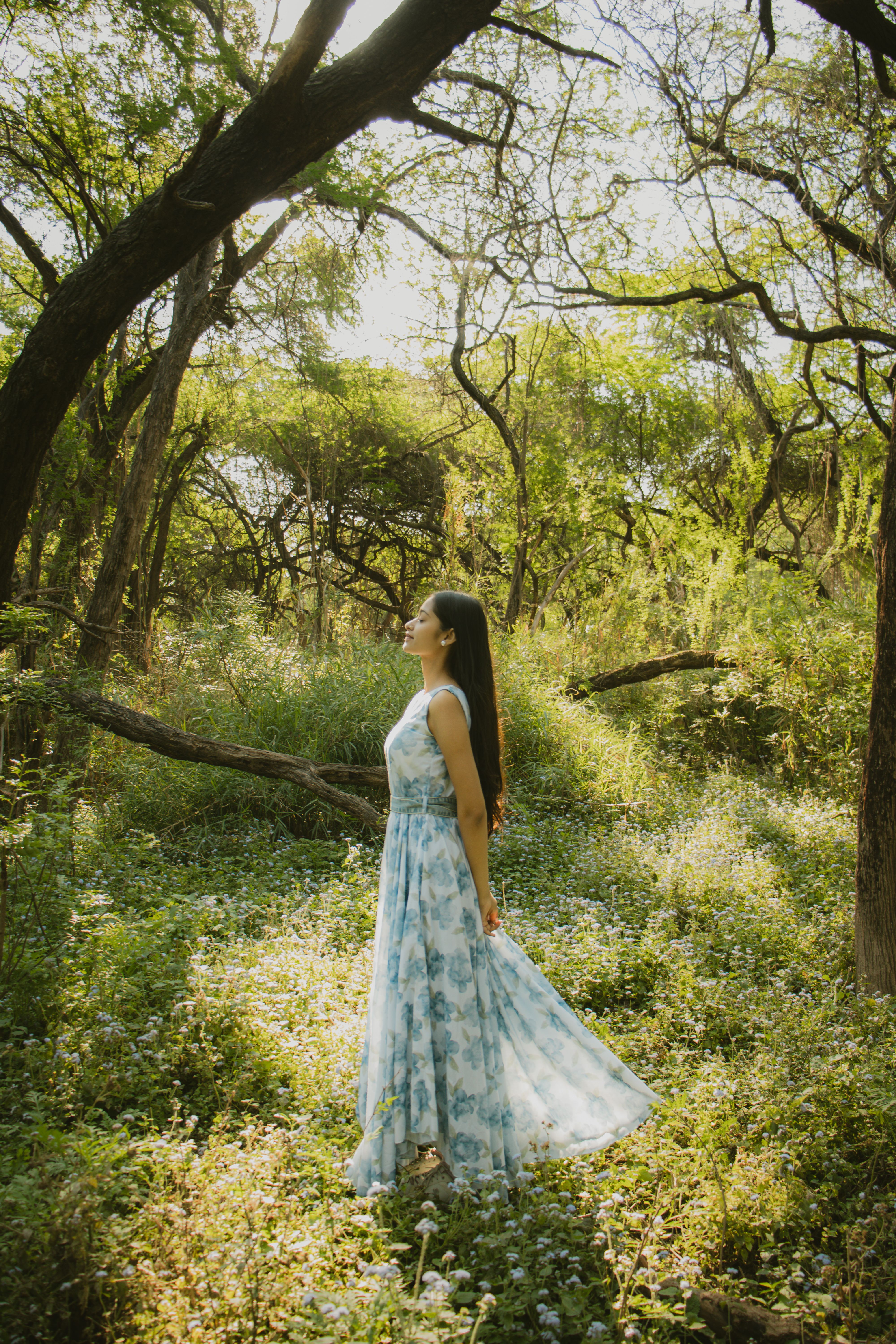 Woman in floral dress basks in sunlight amidst lush green forest.