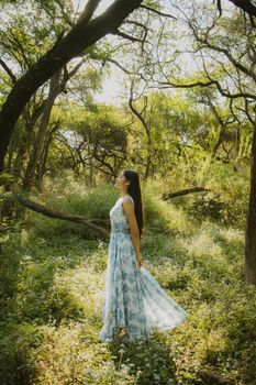 Woman in floral dress basks in sunlight amidst lush green forest.
