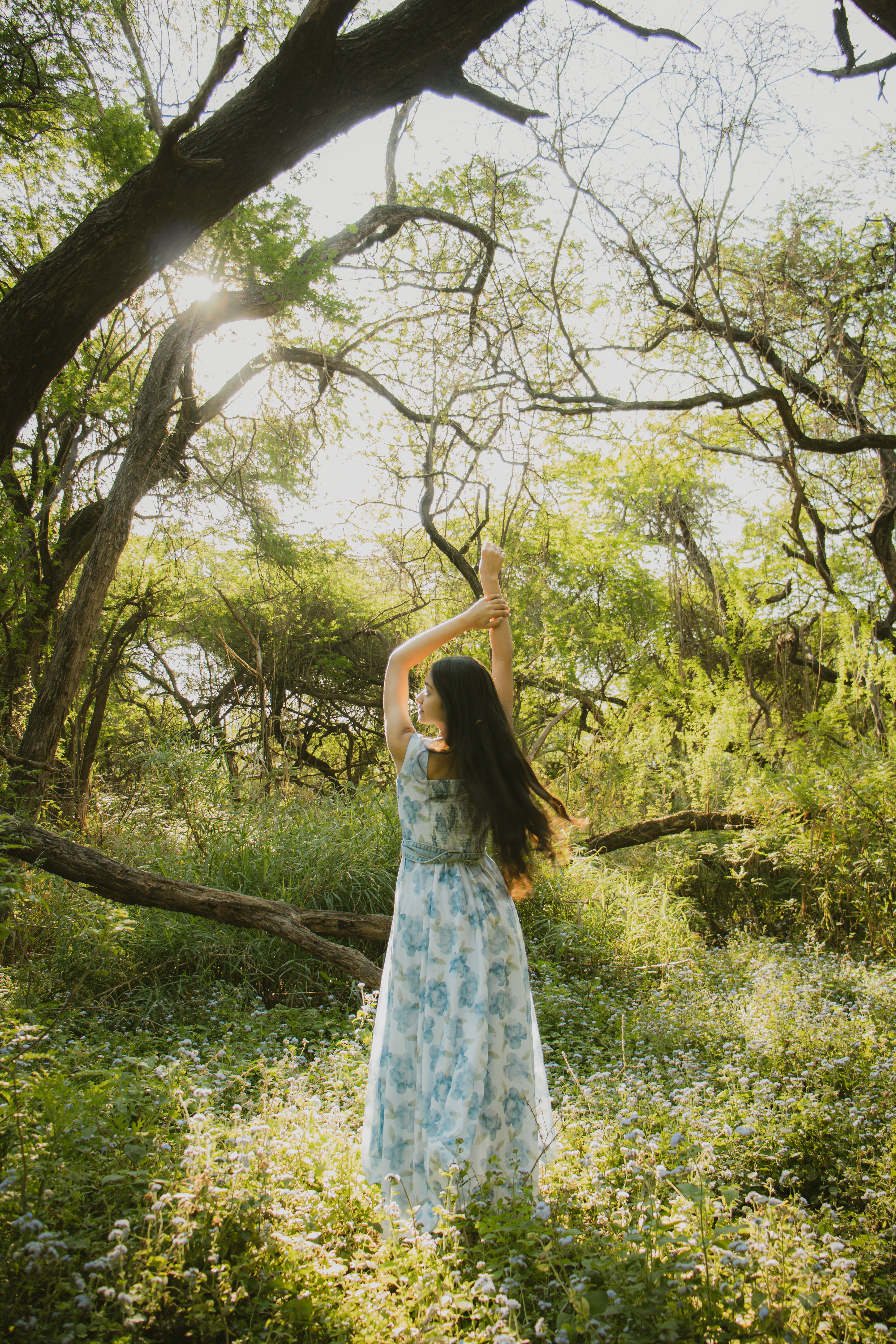A woman freely dancing among sunlit trees in an open forest.