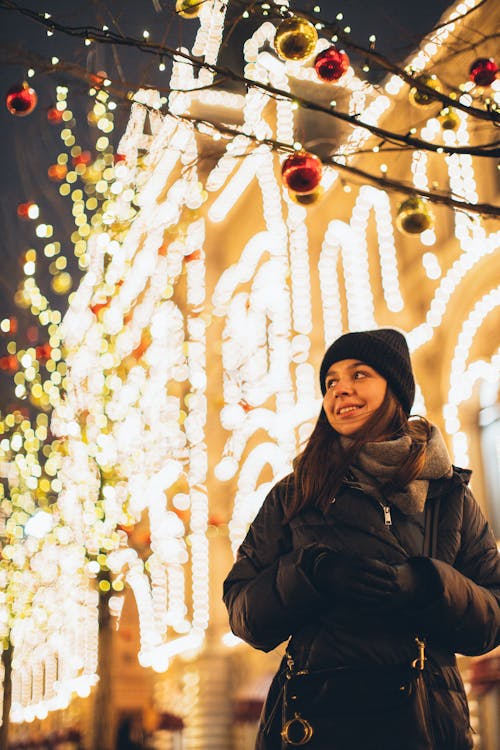Photo of Woman Wearing Black Bubble Jacket and Beanie While Smiling Against Bright Background