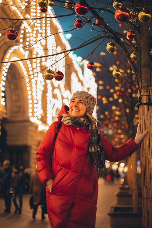 Woman in Red Bubble Jacket Standing Under Christmas Balls