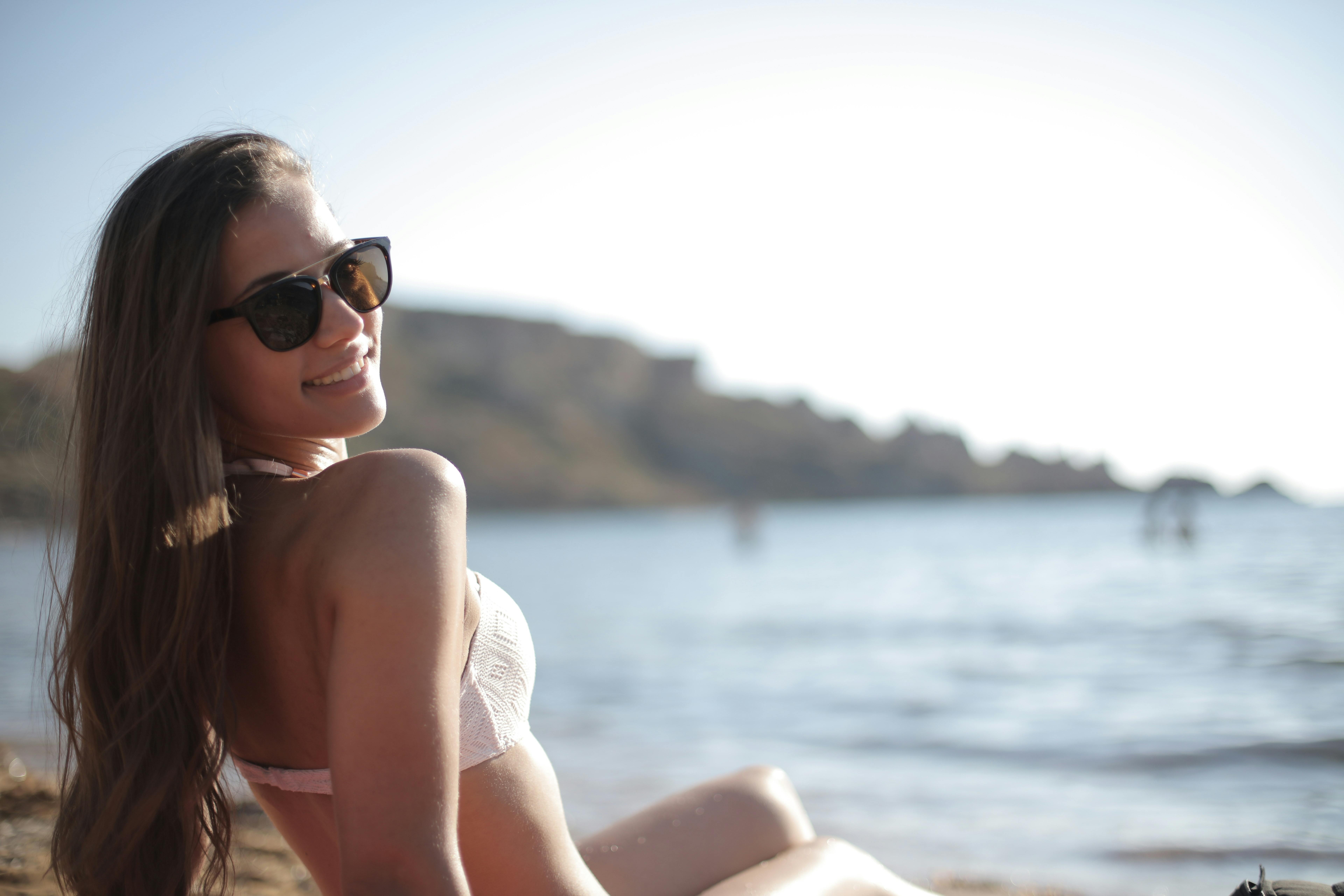 一位戴着太阳镜、穿着比基尼的女子，在海滩上享受了一整天的明媚阳光