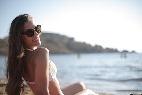 Kobieta W Białym Bikini W Czarnych Okularach Przeciwsłonecznych Siedzi Na Skale W Pobliżu Morza