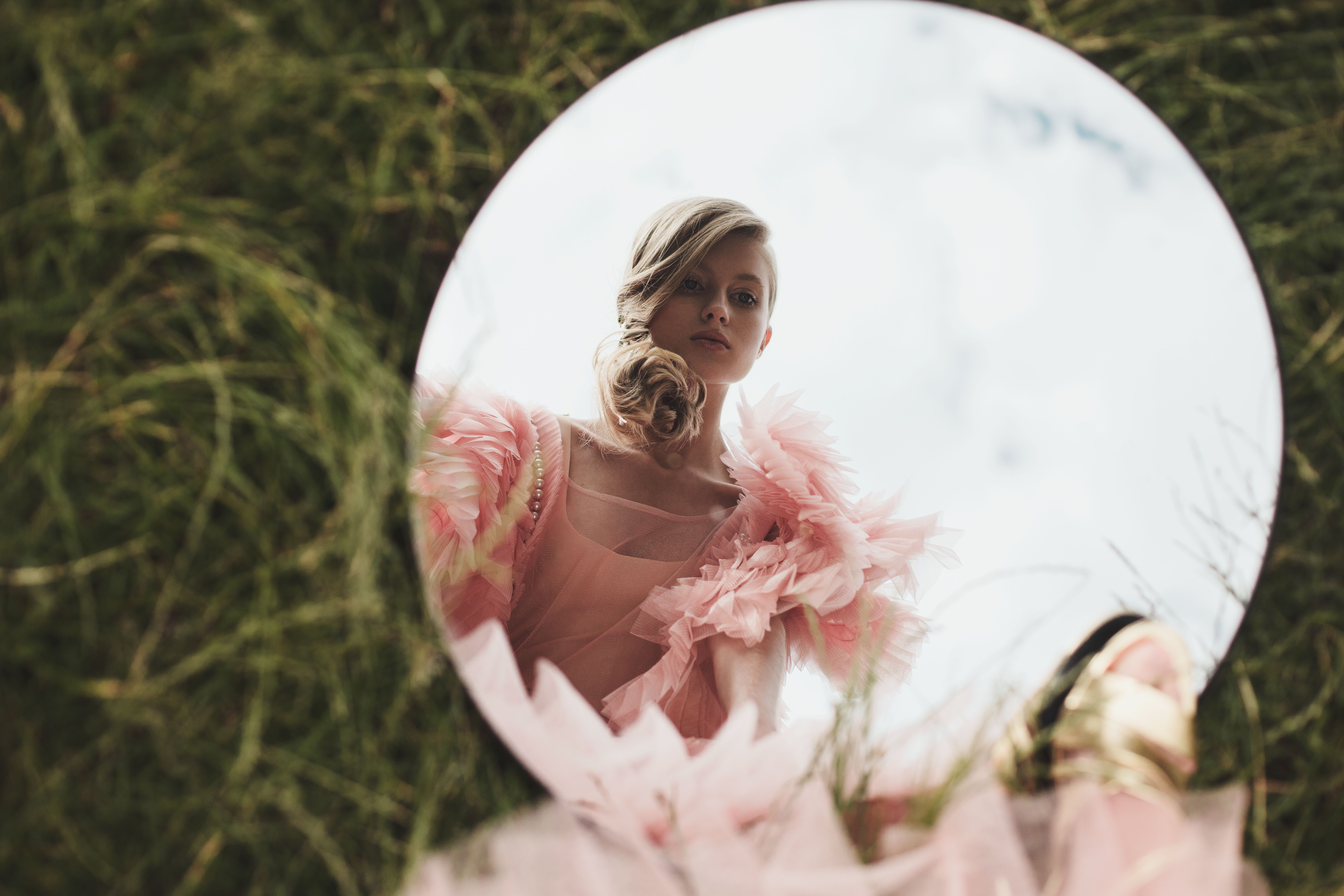 Stylish portrait of a woman in pink, reflected in a circular mirror outdoors.