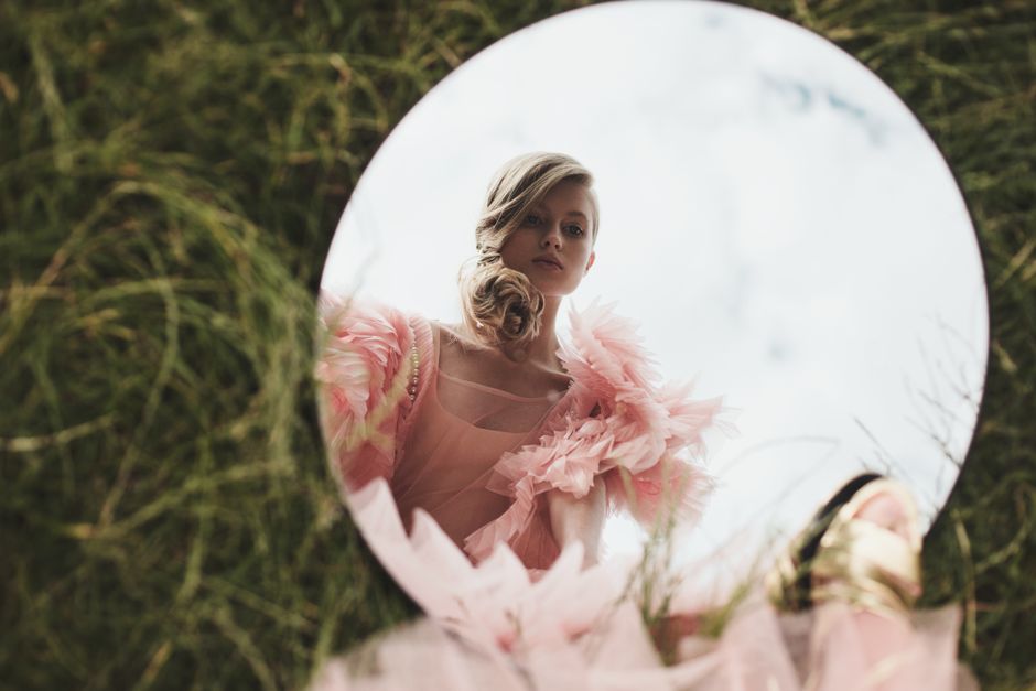 Stylish portrait of a woman in pink, reflected in a circular mirror outdoors.