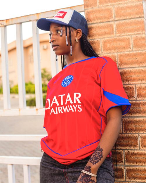 Free Young woman wearing a sports jersey and cap, posing against a brick wall, outdoors. Stock Photo