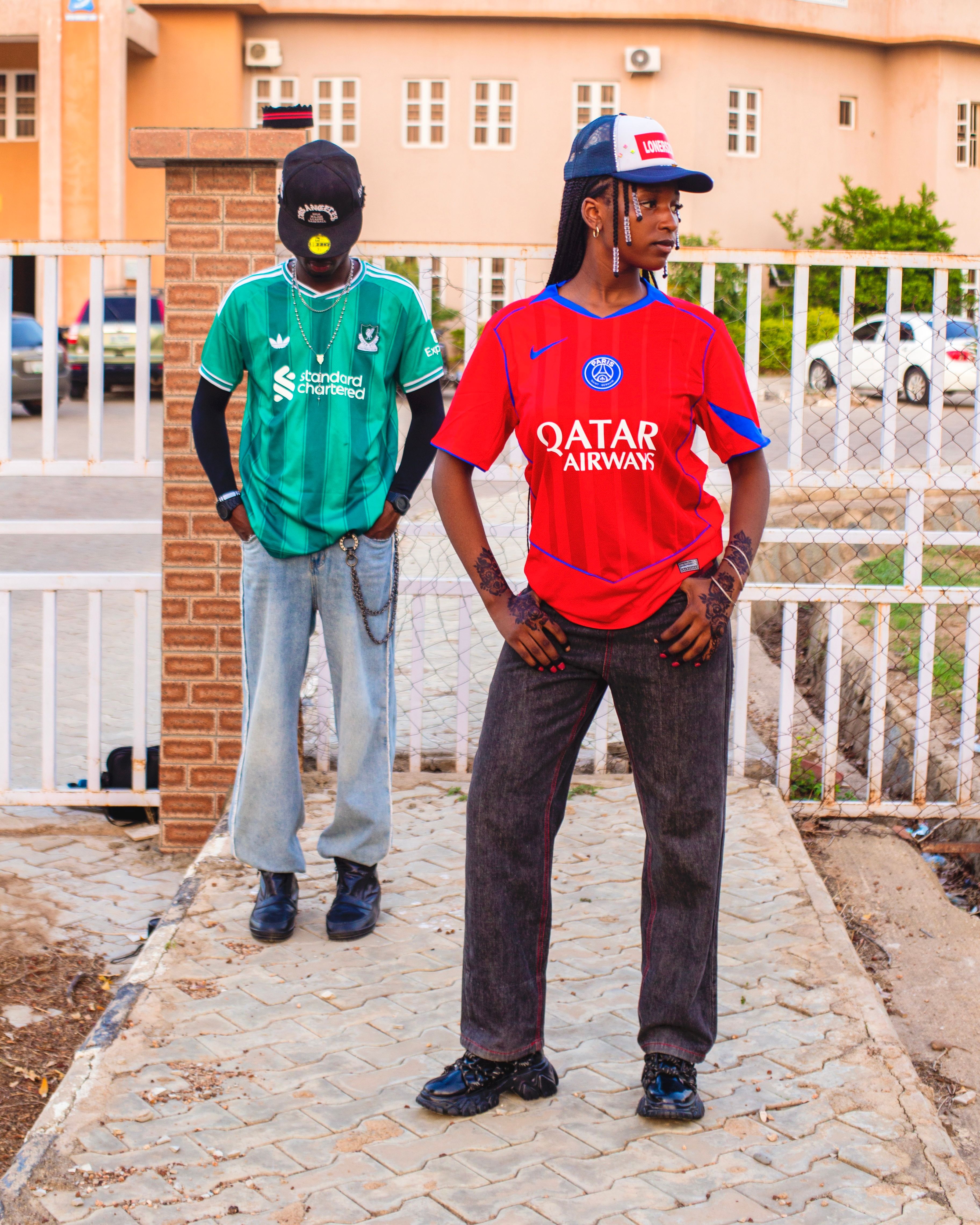 Two individuals in sports jerseys pose outdoors, showcasing modern streetwear style.