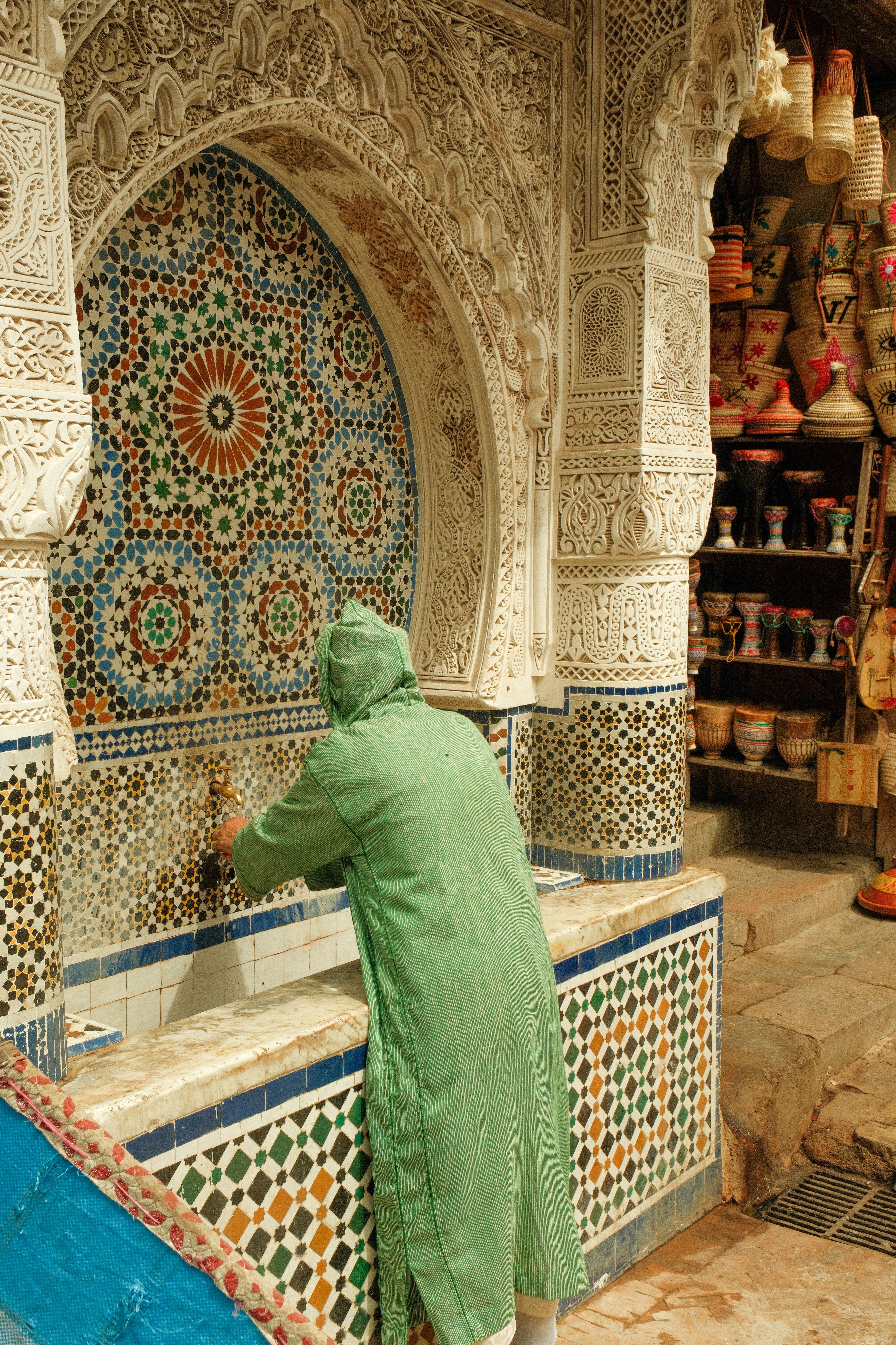 A person washing hands at an ornate Moroccan tile fountain in Fes, showcasing traditional craftsmanship.