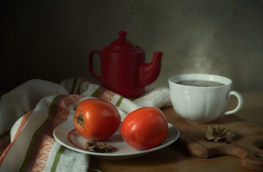 Warm still life featuring a teapot, persimmons, and steaming cup of tea indoors.