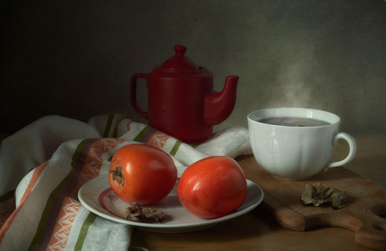 warm still life featuring a teapot persimmons and steaming cup of tea