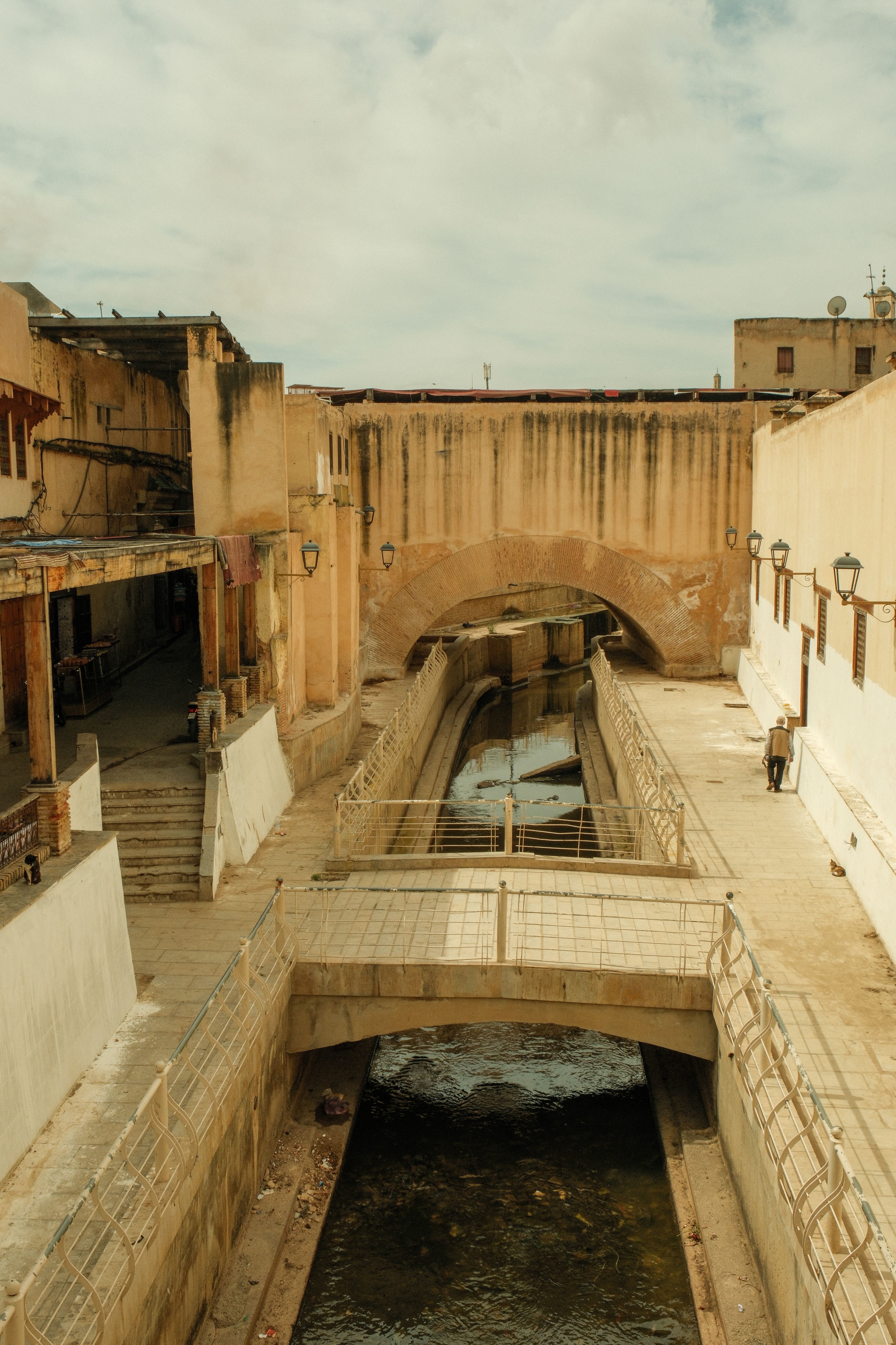 A scenic view of a historic urban canal in Fes, Morocco, showcasing traditional architecture.