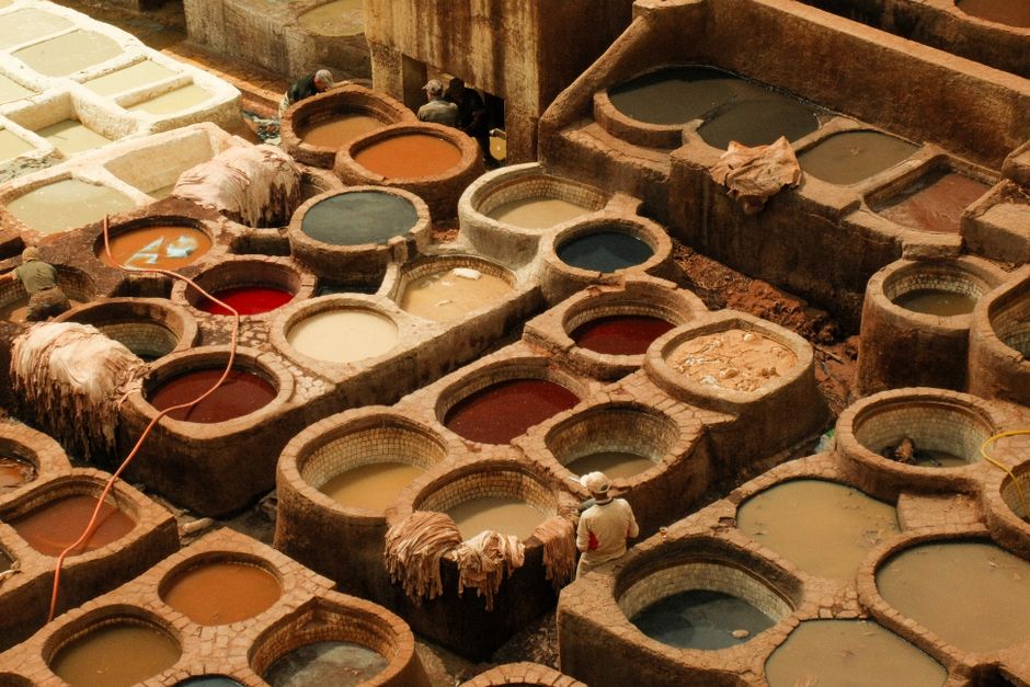 Aerial view of colorful traditional leather tanning vats in Fes, Morocco, with workers in traditional attire.