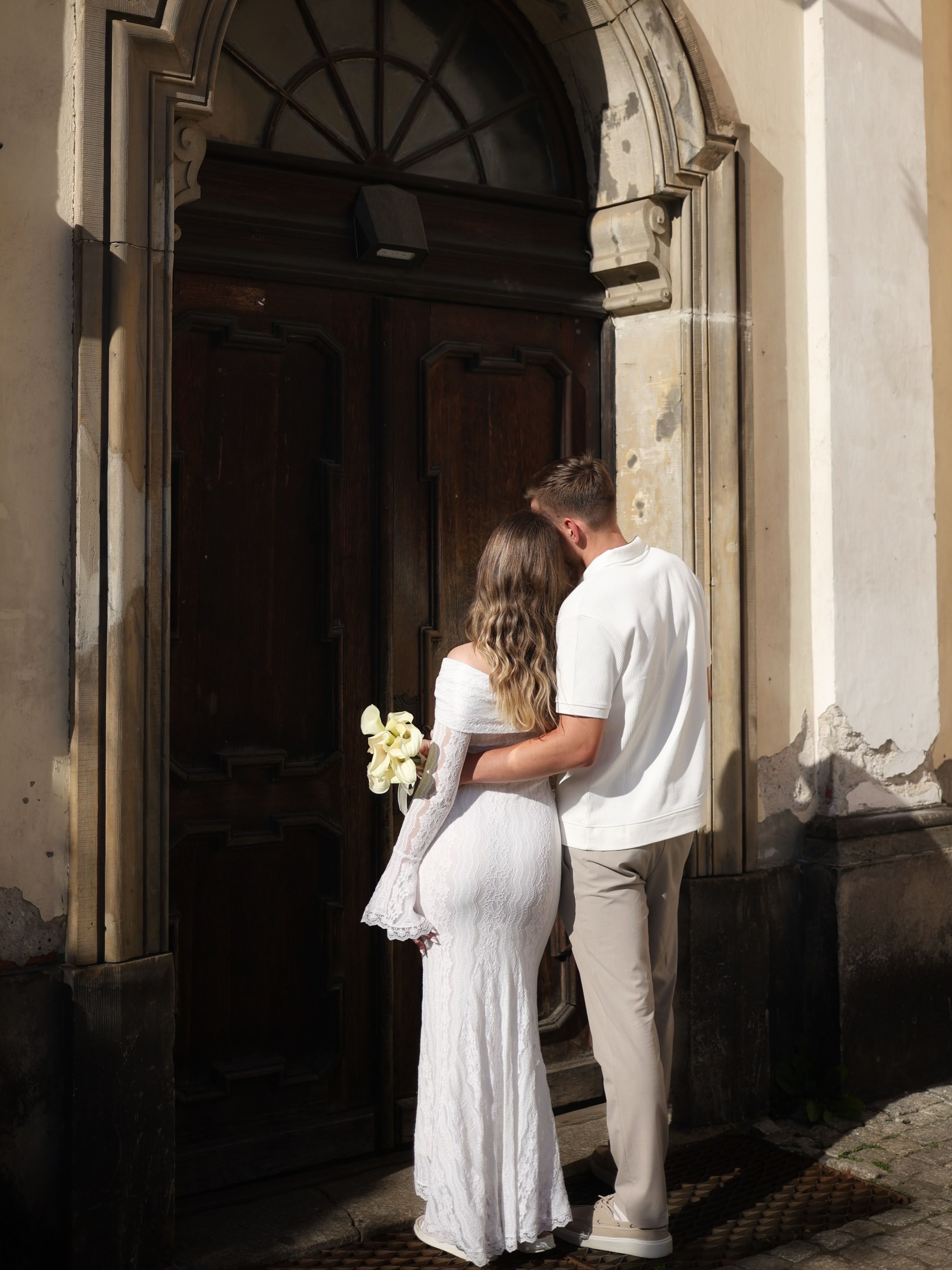 A couple lovingly embraces by an ornate wooden door, suggesting romance and history.