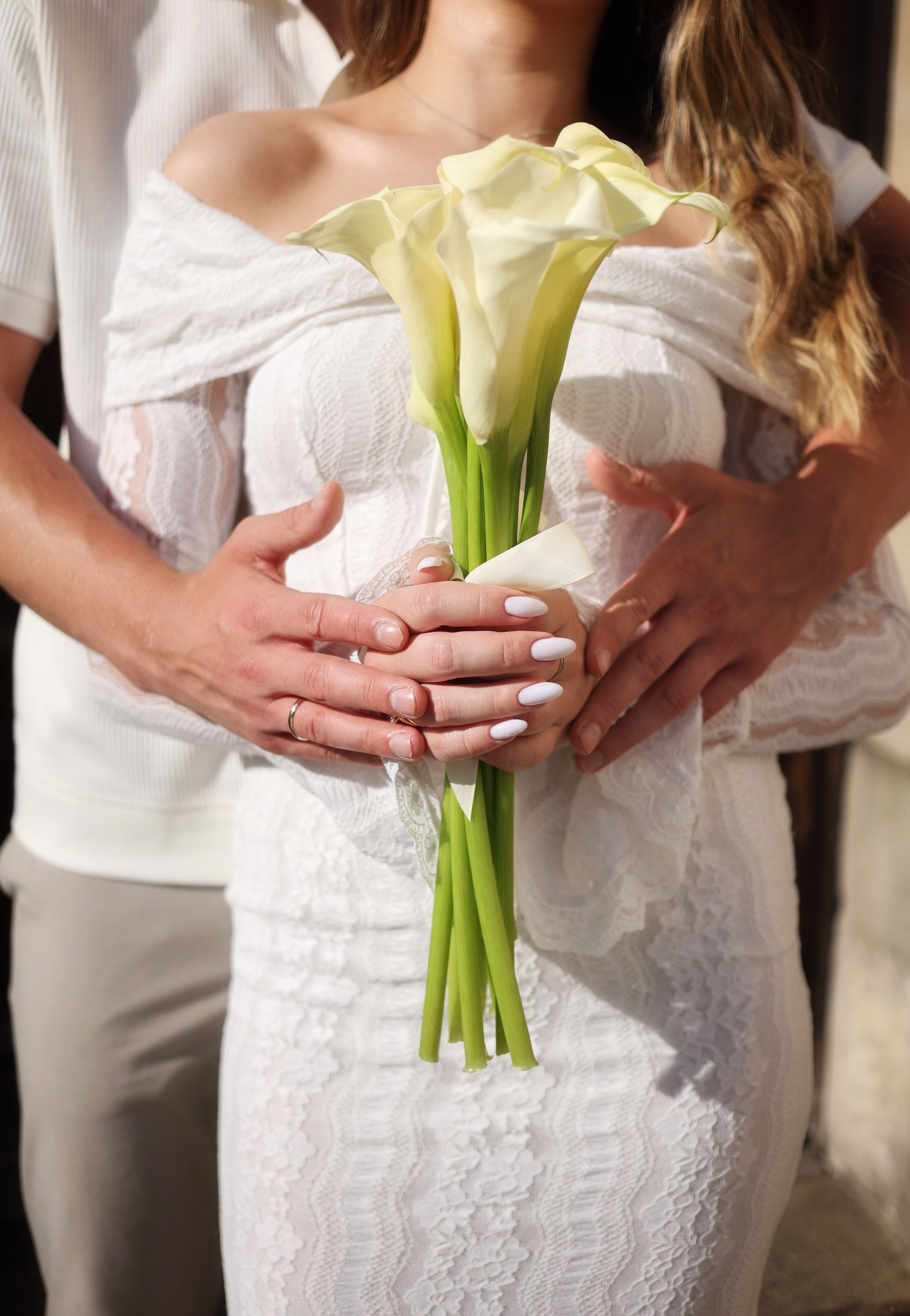 A romantic scene of a couple holding a bouquet of calla lilies on their wedding day.