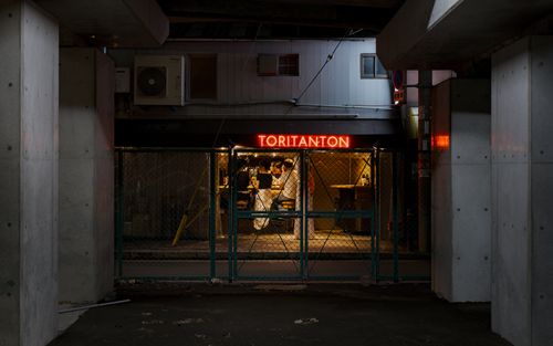 Free A lively scene inside Toritanton bar, Osaka, showcasing urban nightlife through a fence at night. Stock Photo