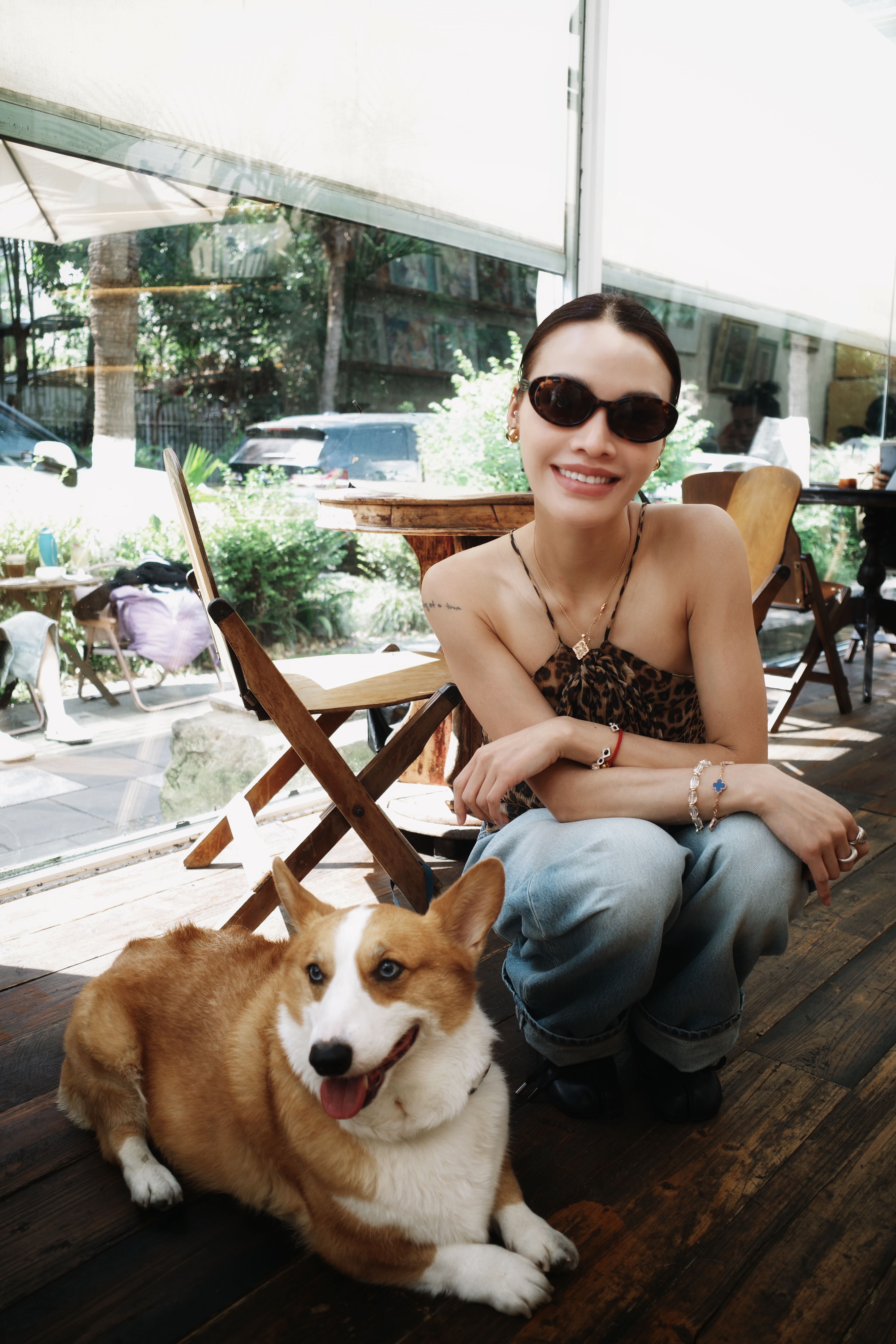 Cheerful woman with sunglasses posing indoors with her pet corgi, creating a warm and friendly atmosphere.