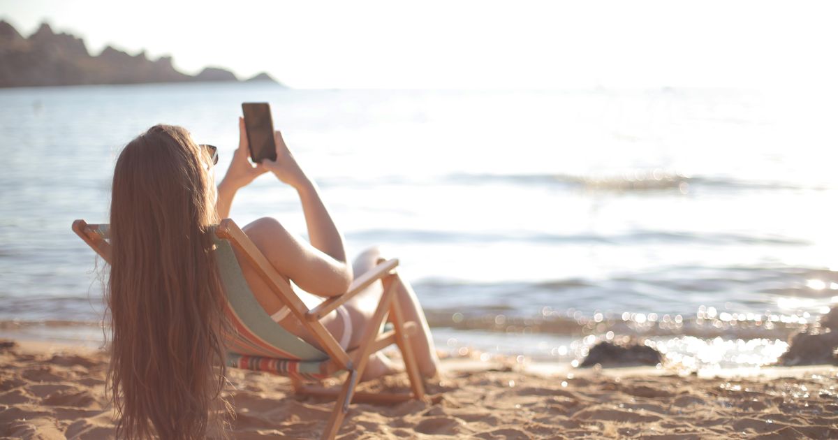 Mulher de biquíni relaxa em uma cadeira de praia à beira do oceano, capturando memórias de verão.