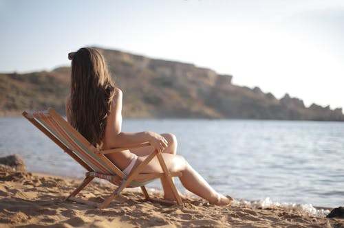 白色比基尼泳裝的婦女坐在海灘的棕色木折疊椅