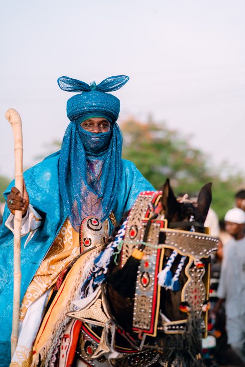 Free A man in traditional blue garments riding a decorated horse during a cultural festival. Stock Photo