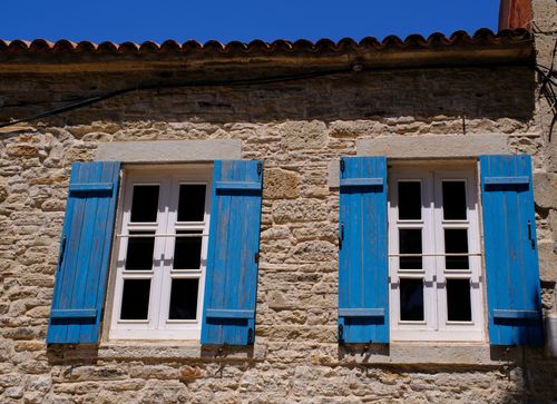 Free Rustic stone house with vibrant blue shutters under a clear sky in Foça, Türkiye. Stock Photo
