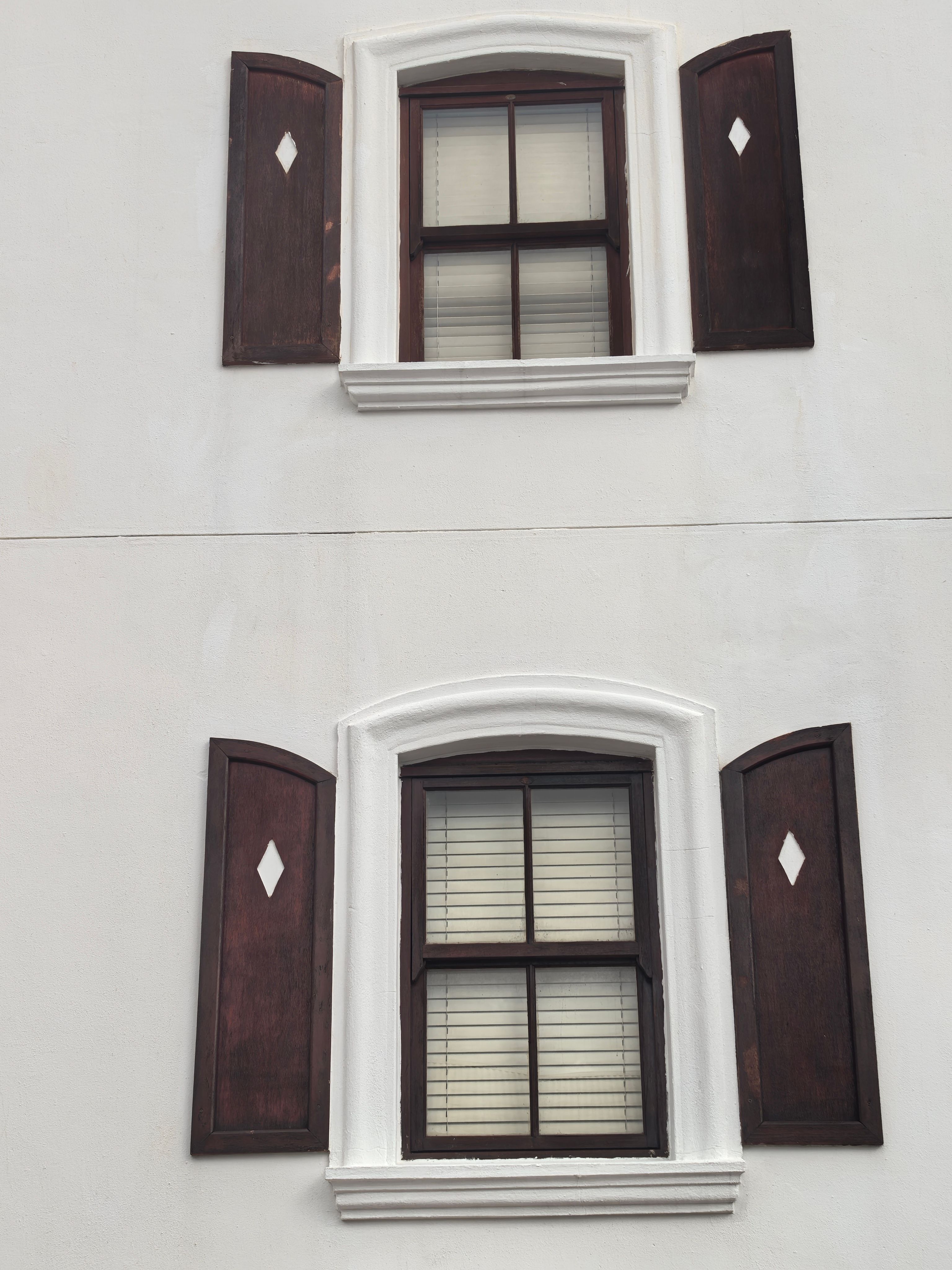 Two rustic windows with wooden shutters on a white wall in Cape Town.