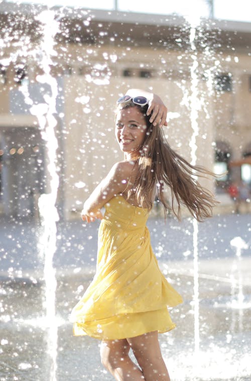 Donna In Vestito Giallo Che Sta Vicino Alla Fontana Di Acqua Mentre Sorride