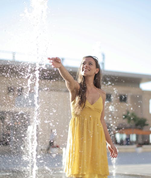 Free Woman in Yellow Sleeveless Dress Standing on Water Fountain Stock Photo