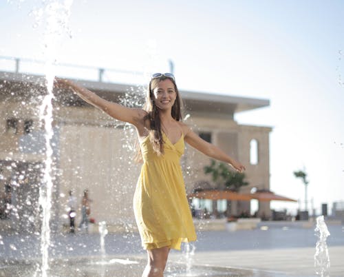 Free Woman in Yellow Dress Standing on Water Fountain Stock Photo