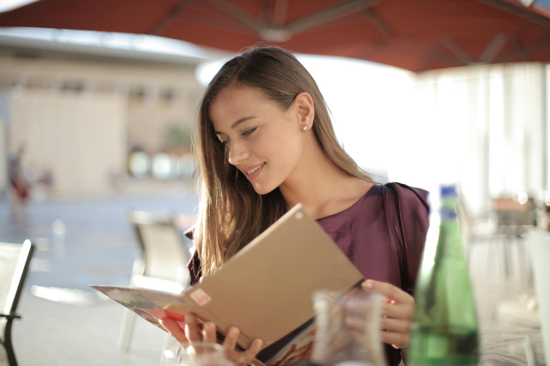 A smiling young woman reading a menu outdoors under parasols, enjoying a casual afternoon.