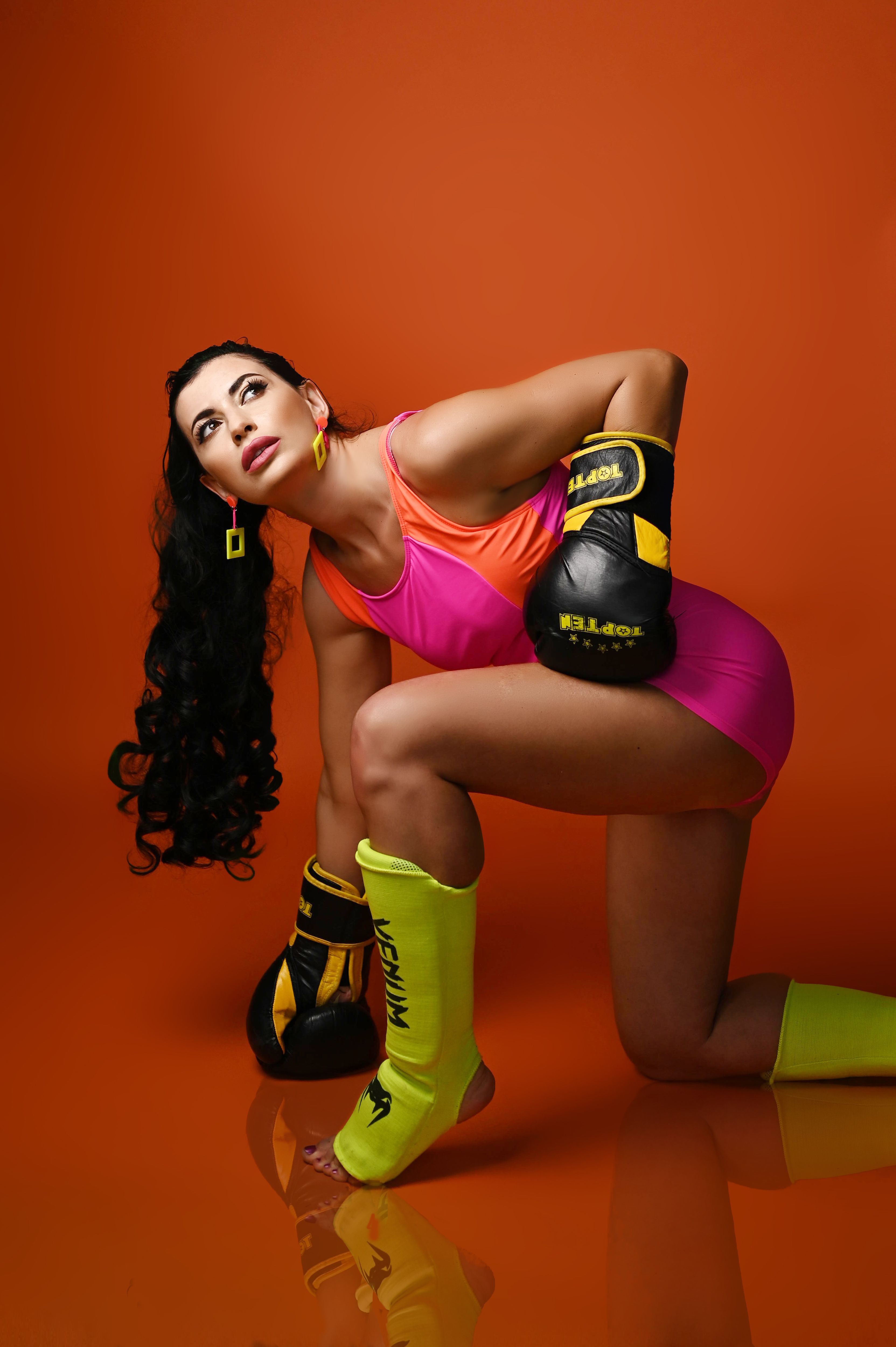 Vibrant portrait of a female boxer in colorful attire on an orange background.