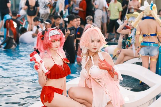 Colorful cosplay characters gather around a pool during a lively outdoor event.
