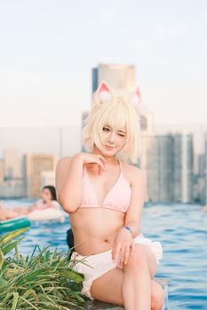 Cosplay model in a playful pose at a rooftop pool with a cityscape in the background.