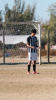 Teen soccer player in black and white uniform stands focused on a sunny outdoor field.