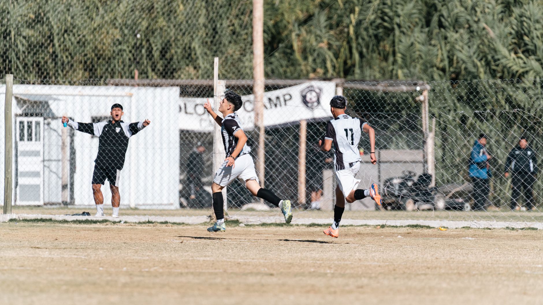 Excited youth soccer players celebrate a goal during a daytime match on an outdoor field.