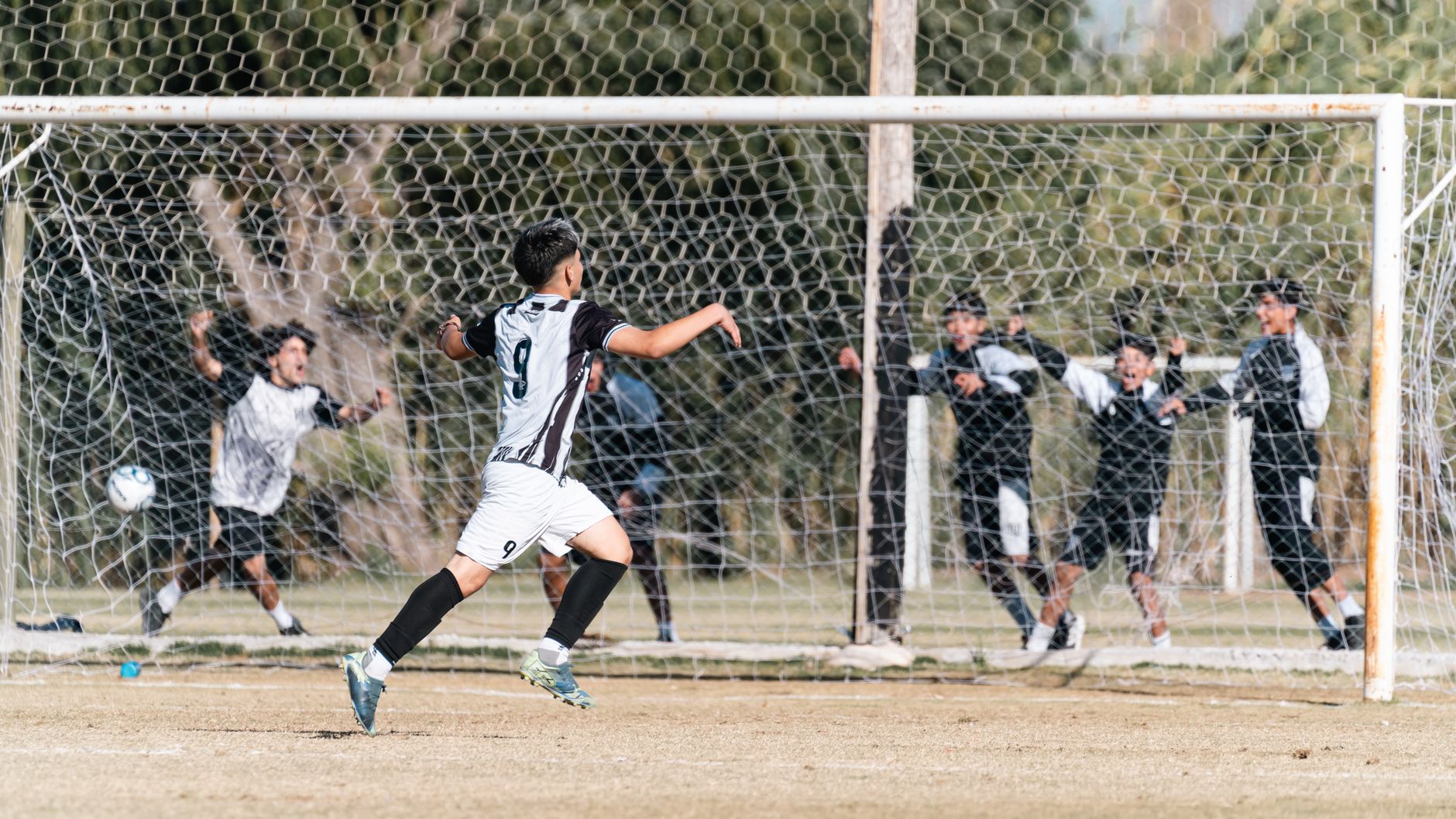 A soccer player in white uniform celebrates scoring a goal outdoors.