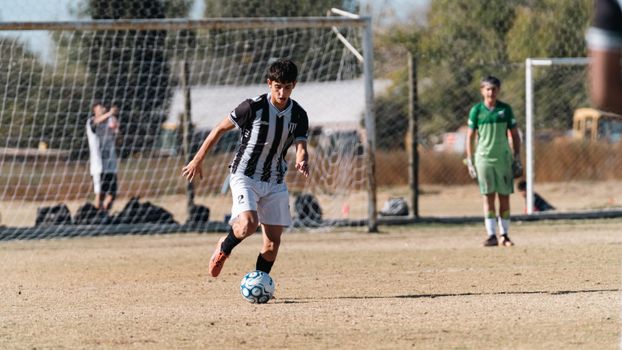 Young soccer player dribbling towards goal on a sunny day in a competitive match.