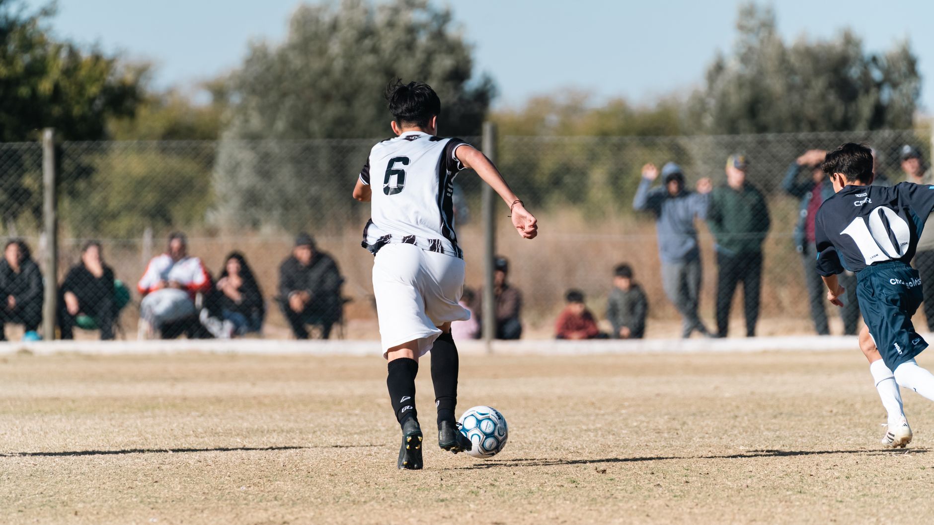 Young soccer players in action on a sunny outdoor field with spectators.