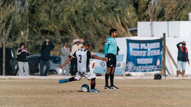 Soccer player taking a powerful kick during an outdoor match with referee observing.