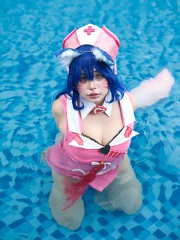 A cosplayer dressed in a pink nurse costume poses in a pool, showcasing vibrant style.