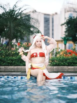 A young woman in cosplay attire posing by the poolside with urban background.