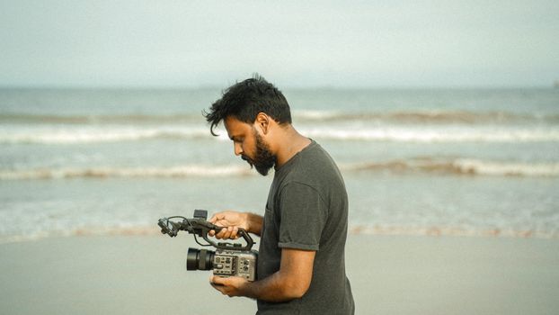 A young man holding a professional camera on the beach in Kakinada, India.