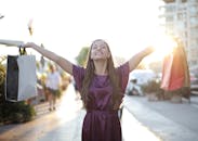 一个快乐的女人提着购物袋，在阳光明媚的日子里兴奋地举起双臂