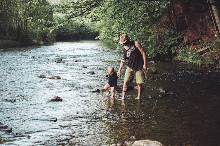 Photo Of Man Holding His Child While Walking In The River