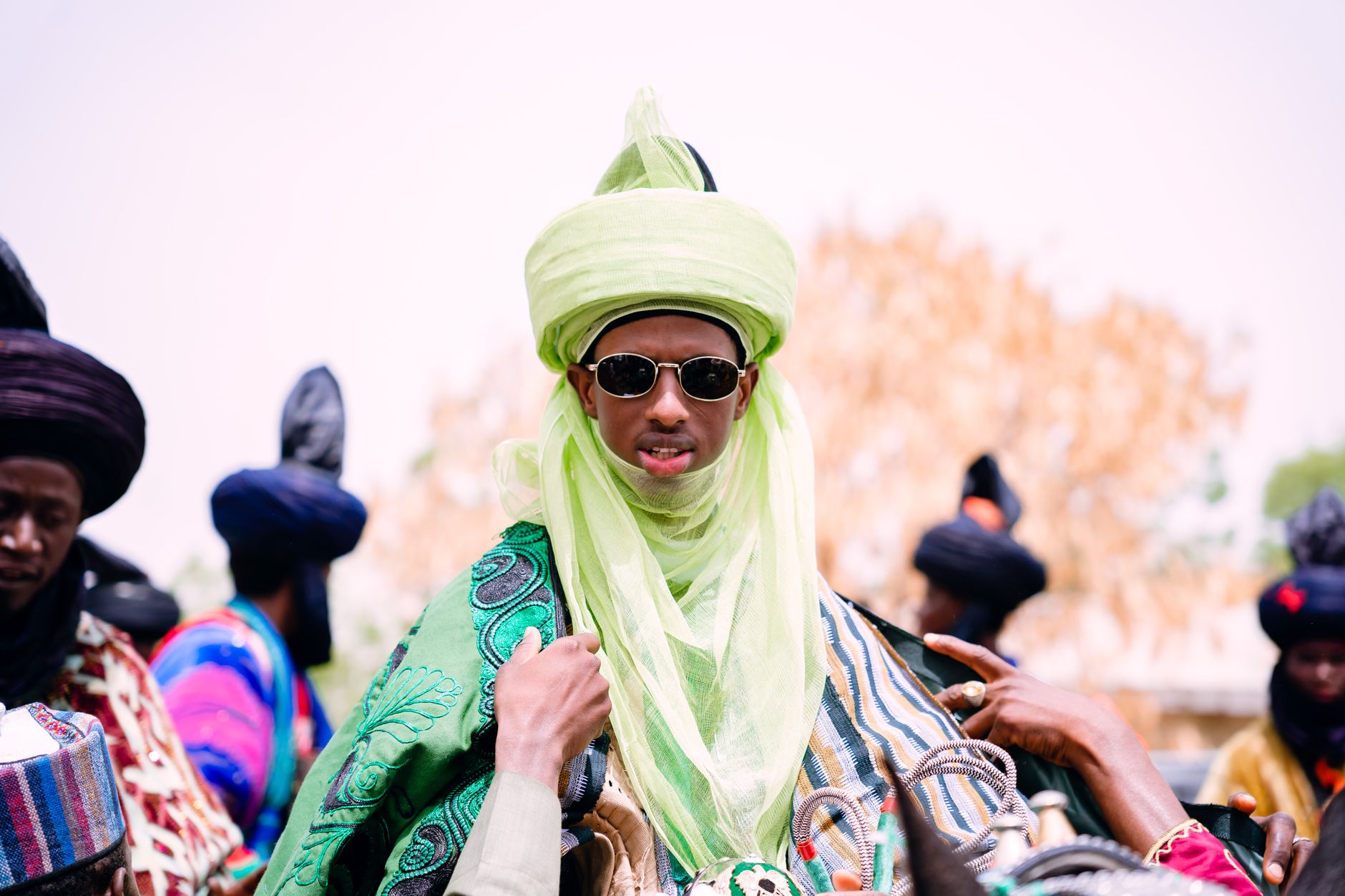 Vibrant celebration featuring traditional African attire and headwear in a sunny outdoor setting.