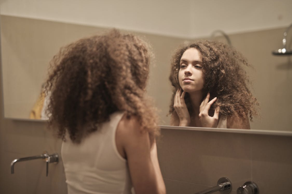Free Woman in White Tank Top While Looking Herself at a Mirror Stock Photo