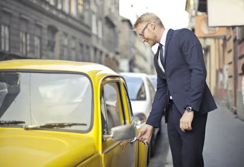 Man in Black Suit Standing Beside Yellow Car