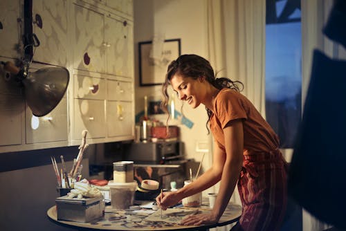 Фотография женщины, которая рисует, улыбаясь и стоя у стола
