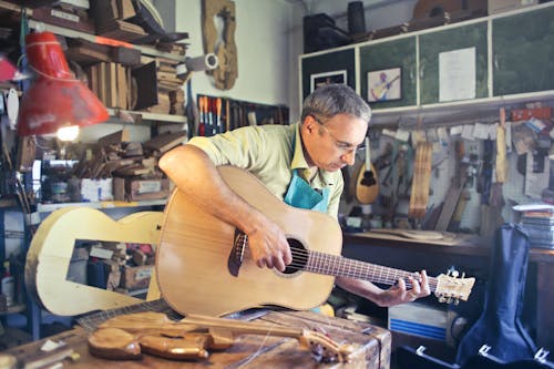 Человек в желтой рубашке поло играет на коричневой акустической гитаре
