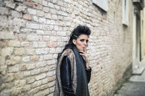 Free Photo of Woman Wearing Fur Coat While Smoking Near Brick Wall Stock Photo